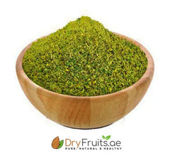 Wooden bowl filled with green pistachio flour on a white background, branded with 'DryFruits.ae'.